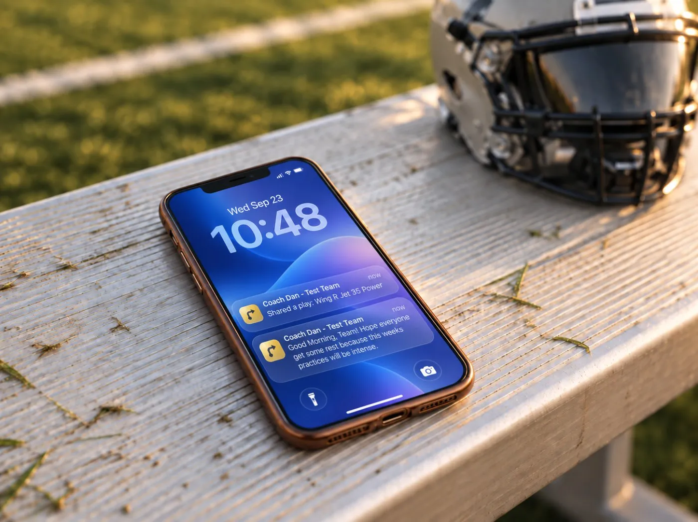 A phone on a bleacher bench showing a PlaybookMax notification from Coach Dan to the whole team